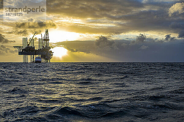 Offshore-Bohrplattform bei Sonnenaufgang mit Arbeitsschiff