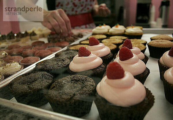 Ein Cupcake-Ladenbesitzer dekoriert Cupcakes  die zum Verkauf bereitstehen.