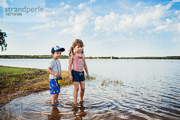 Junge und Mädchen stehen mit Ferngläsern im Wasser am See
