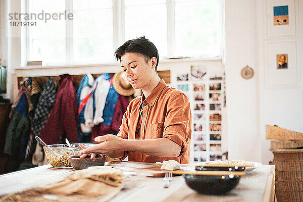 Androgyne Asiatin bereitet zu Hause Knödel auf einem Holztisch zu