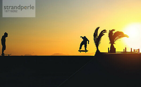 Silhouette eines jungen springenden Skateboardfahrers beim Reiten  Sommersonnenuntergang