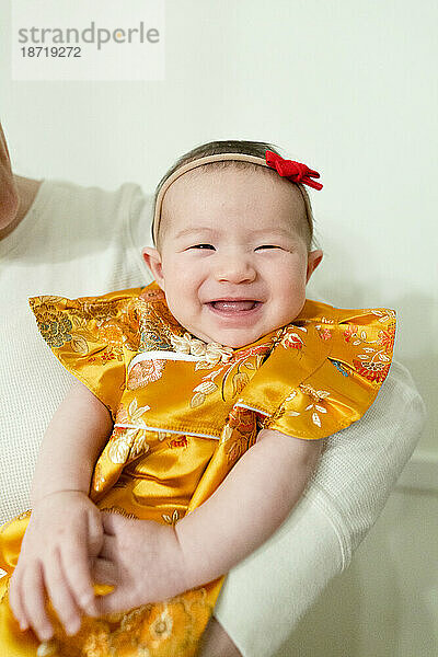 Fröhliches und lächelndes Baby  das ein traditionelles gelbes Kleid für eine Party trägt