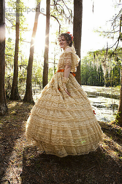 Eine junge Frau posiert in einem Southern-Belle-Outfit  darunter ein großes  reich verziertes historisches Kleid  in der Nähe eines Sees.