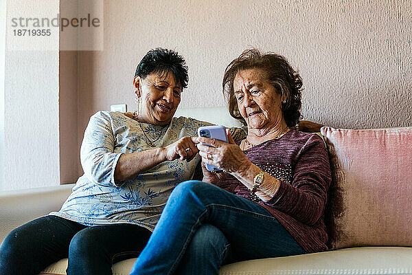 Zwei alte Frauen schauen auf das Smartphone und sitzen auf dem Sofa