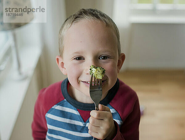 Junge isst spielerisch Brokkoli und lächelt