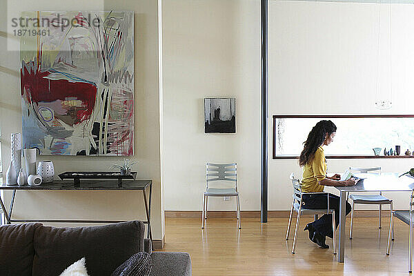Eine asiatisch-amerikanische Frau sitzt auf einem Stuhl und liest in einem modernen Haus in Del Mar  Kalifornien.