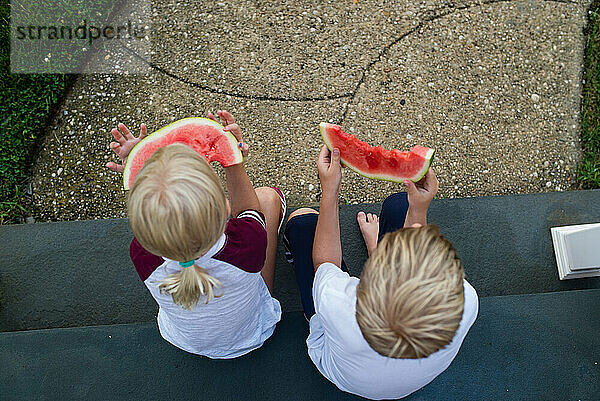 Oben: Jungen und Mädchen  die draußen auf einer Treppe Wassermelone essen