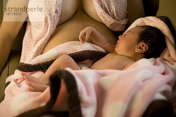 Ein Neugeborenes schläft neben den bedeckten Brüsten seiner Mutter