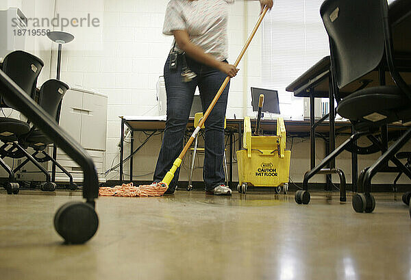 A female janitor sweeps the floor with a broom and dustpan in a historic shopping mall  (low angle).