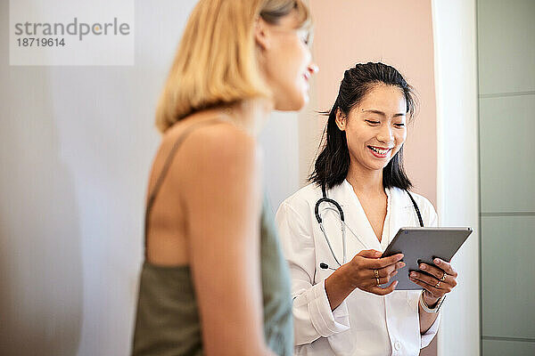 Lächelnder Arzt benutzt Tablet-PC  während er mit einer Patientin sitzt