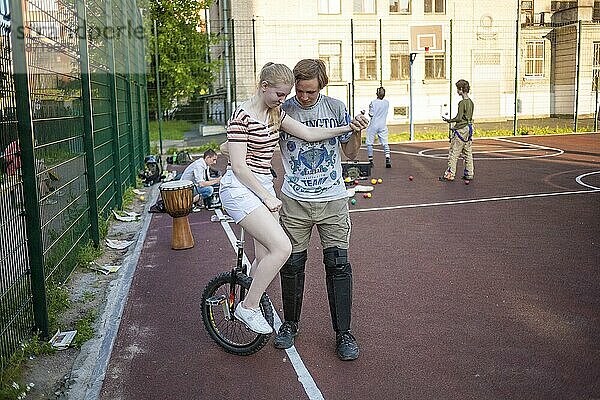 Ein Junge hilft einem Mädchen  auf einem Einrad im Stadtpark zu balancieren