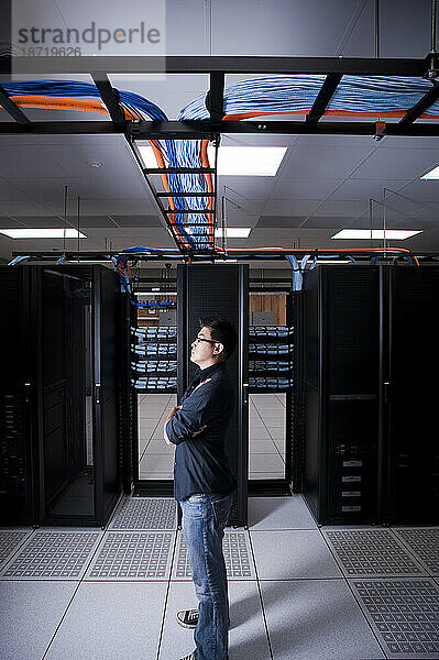 Ein junger erwachsener asiatischer Mann wird vor einem Netzwerk-Computerserver porträtiert.