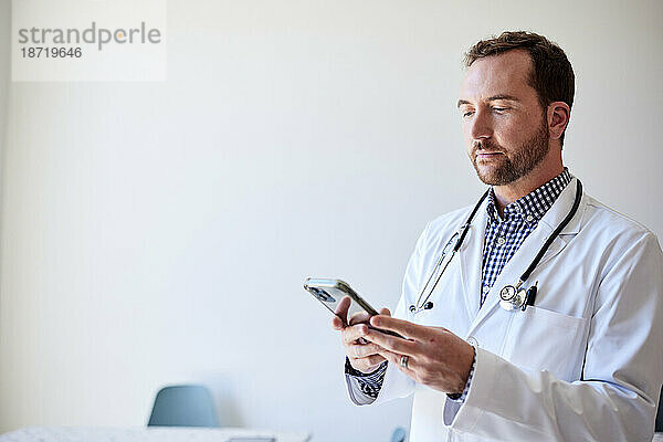 Männlicher Mitarbeiter im Gesundheitswesen nutzt Smartphone  während er in der Klinik steht