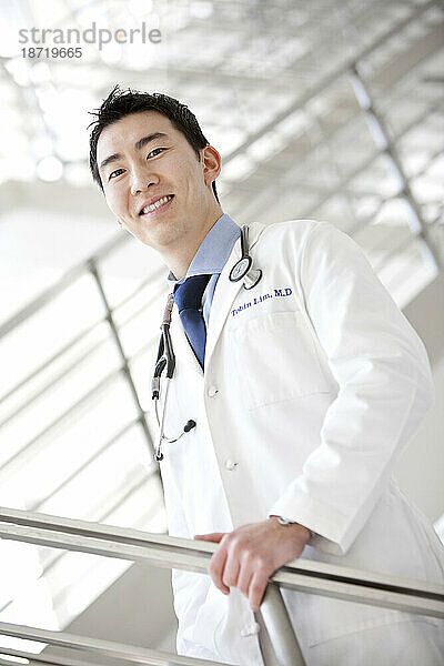 Ein Porträt eines lächelnden männlichen Arztes in einem weißen Laborkittel mit einem Stethoskop um den Hals.