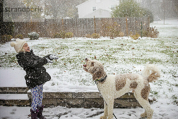 Kleines Mädchen spielt lächelnd mit einem großen Hund draußen im Schnee