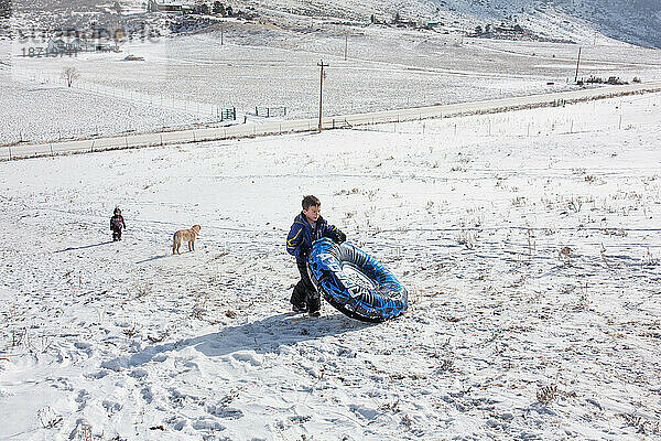 Jungen und Hund laufen mit Schneeschlauch den Rodelhang hinauf
