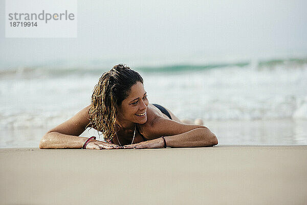 Frau mit Bikini lächelt und sonnt sich am Strand.