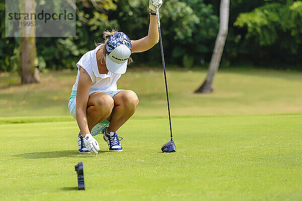 In voller Länge zeigt eine junge Frau einen Golfball auf dem Abschlag