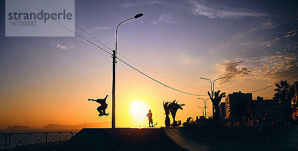 Silhouette eines jungen springenden Skateboardfahrers beim Reiten  Sommersonnenuntergang.