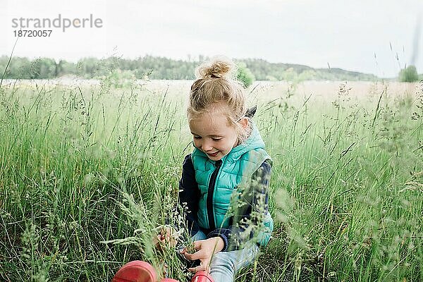 Junges Mädchen sitzt lächelnd und glücklich auf einem Feld
