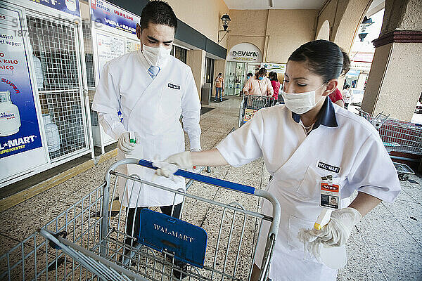 Zwei Personen mit Masken reinigen einen Einkaufswagen im Supermarkt  bevor die Kunden diese als Schutz gegen die Schweinegrippe mitnehmen