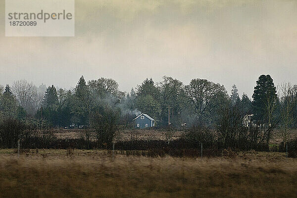 Von der Autobahn in der Nähe von Seattle  Washington  aus ist ein blaues Bauernhaus zu sehen  das im Winter von Bäumen umgeben ist.