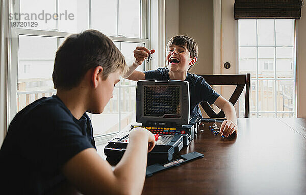 Junge lacht über seinen Bruder  während sie zusammen ein Brettspiel spielen.