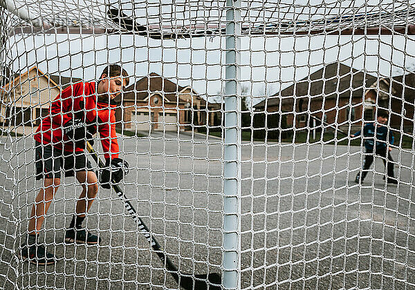 Bild von zwei Jungen  die Straßenhockey spielen  aufgenommen durch ein Hockeynetz.