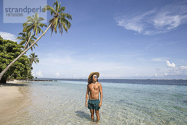 Gebräunter junger Mann  am Sandstrand mit klarem  blauem Wasser und Palmen