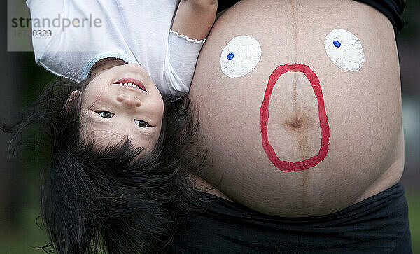 Ein Kind spielt mit einer Mutter mit schwangerem Bauch
