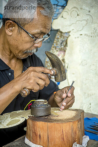 Mann stellt in der Werkstatt traditionelle Schattenpuppen mit Leder und Hammer her