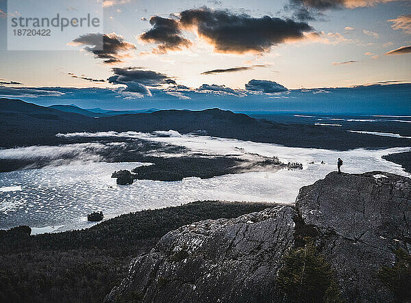 Einsamer Wanderer steht auf einem felsigen Gipfel mit Seen und Bergen  Sonnenaufgang