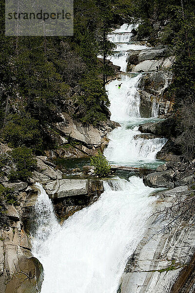 Ein männlicher Kajakfahrer rennt einen großen Wasserfall inmitten vieler anderer großer Wasserfälle entlang.