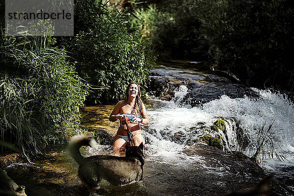 Blonde Frau badet in einem schönen Fluss mit einem Siberian Husky-Hund.