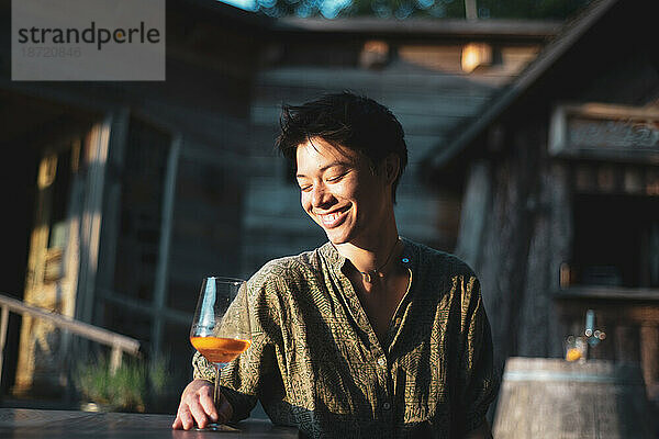 Eine asiatische Person lächelt glücklich mit einem Getränk im Sonnenlicht im Holzcafé