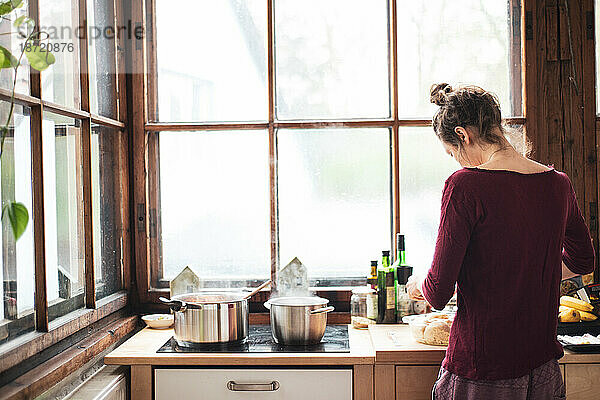 Junge Frau kocht zu Hause in einer natürlichen Holzküche mit großem Fenster