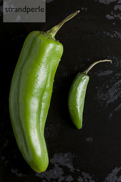 Zwei Arten scharfer grüner Bio-Paprika liegen auf einem nassen schwarzen Schneidebrett in einer heimischen Küche in Seattle  Washington.