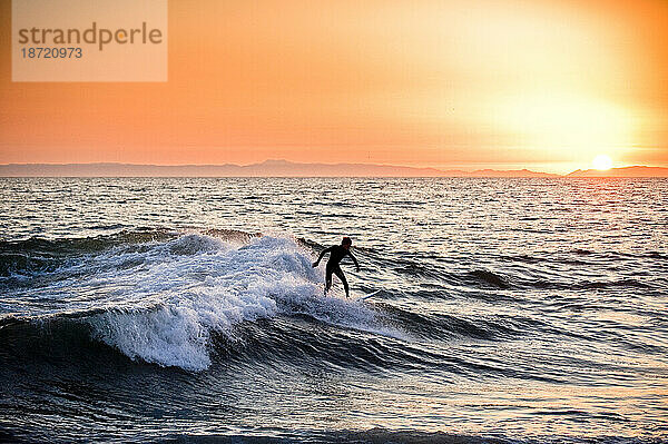 Ein junger Mann surft bei Sonnenuntergang.