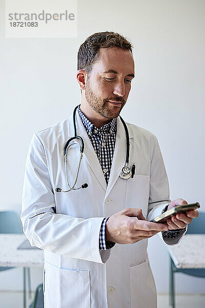 Männlicher Arzt surft mit Smartphone im Internet  während er in der Klinik steht