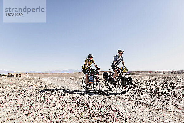 Zwei lächelnde kaukasische Radfahrer fahren auf einer unbefestigten Wüstenstraße in Marokko