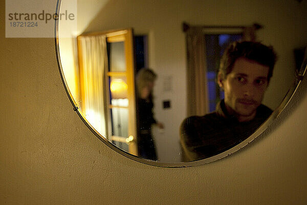 Ein Mann blickt durch einen Spiegel zurück  als eine Frau den Raum betritt. (Selektiver Fokus)
