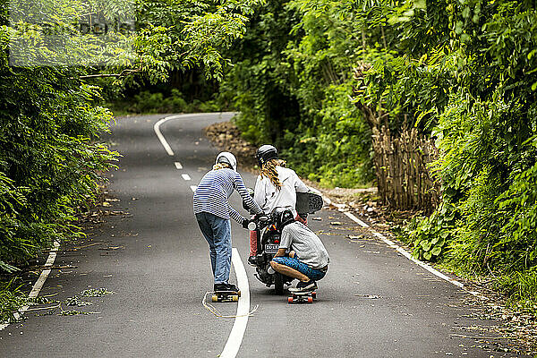 Zwei Longboarder tragen ein Motorrad und einen dritten Skateboarder