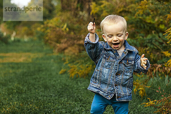 Ein lachender kleiner Junge hält einen Stock in der Hand und spielt draußen im Herbst