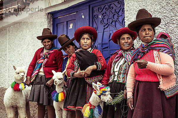 Einheimische Frauen lachen in traditioneller farbenfroher Kleidung mit Alpakas