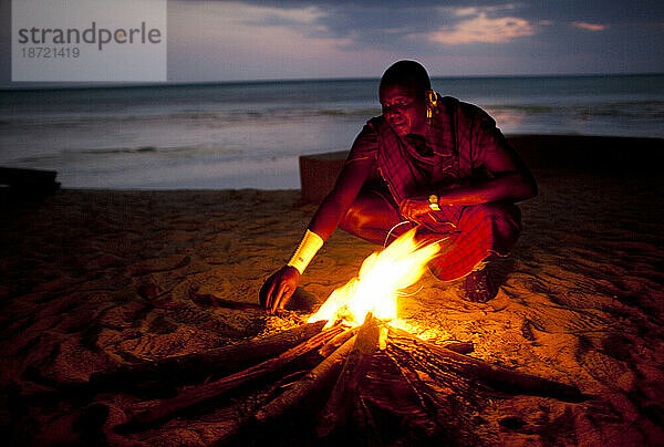 Ein Mitglied des Massai-Stammes im Norden Tansanias  der als Wächter für örtliche Hotels arbeitet  kümmert sich um ein Lagerfeuer am Strand.