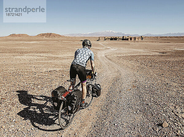 Ein Radfahrer fährt durch eine Wüste in Richtung Ruinen  Ouarzazate  Marokko