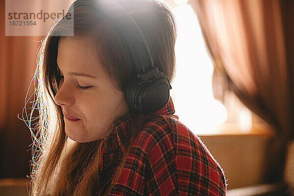 Fröhliches Teenager-Mädchen mit geschlossenen Augen  das über Kopfhörer Musik hört