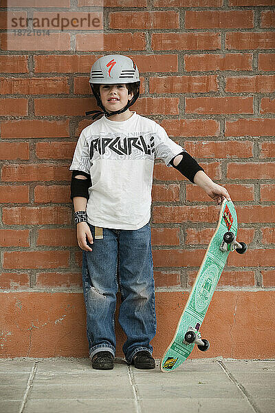 Ein Kind steht mit seinem Skateboard an einer Ziegelwand. Esquel  Chubut  Argentinien.