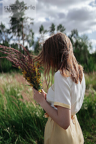 Eine junge Frau steht mit einem Blumenstrauß im hohen Gras