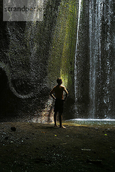 Ein Mann in einer Höhle blickt auf einen Wasserfall. Bali.